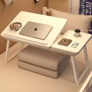Bureau pliable Workphile posé sur un lit, plateau incliné avec ordinateur portable, casque et café